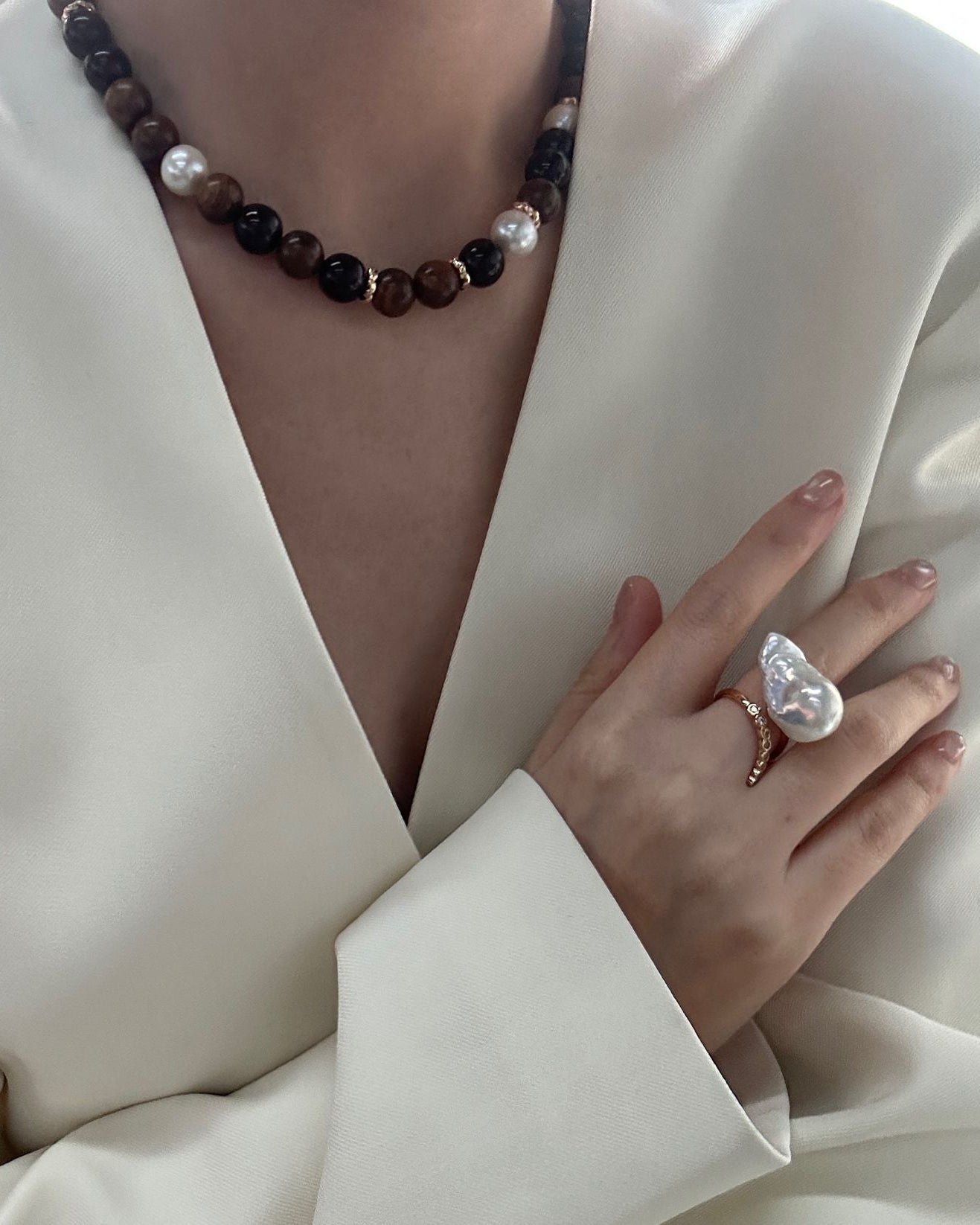 Person wearing a necklace and holding a pearl ring against a white background