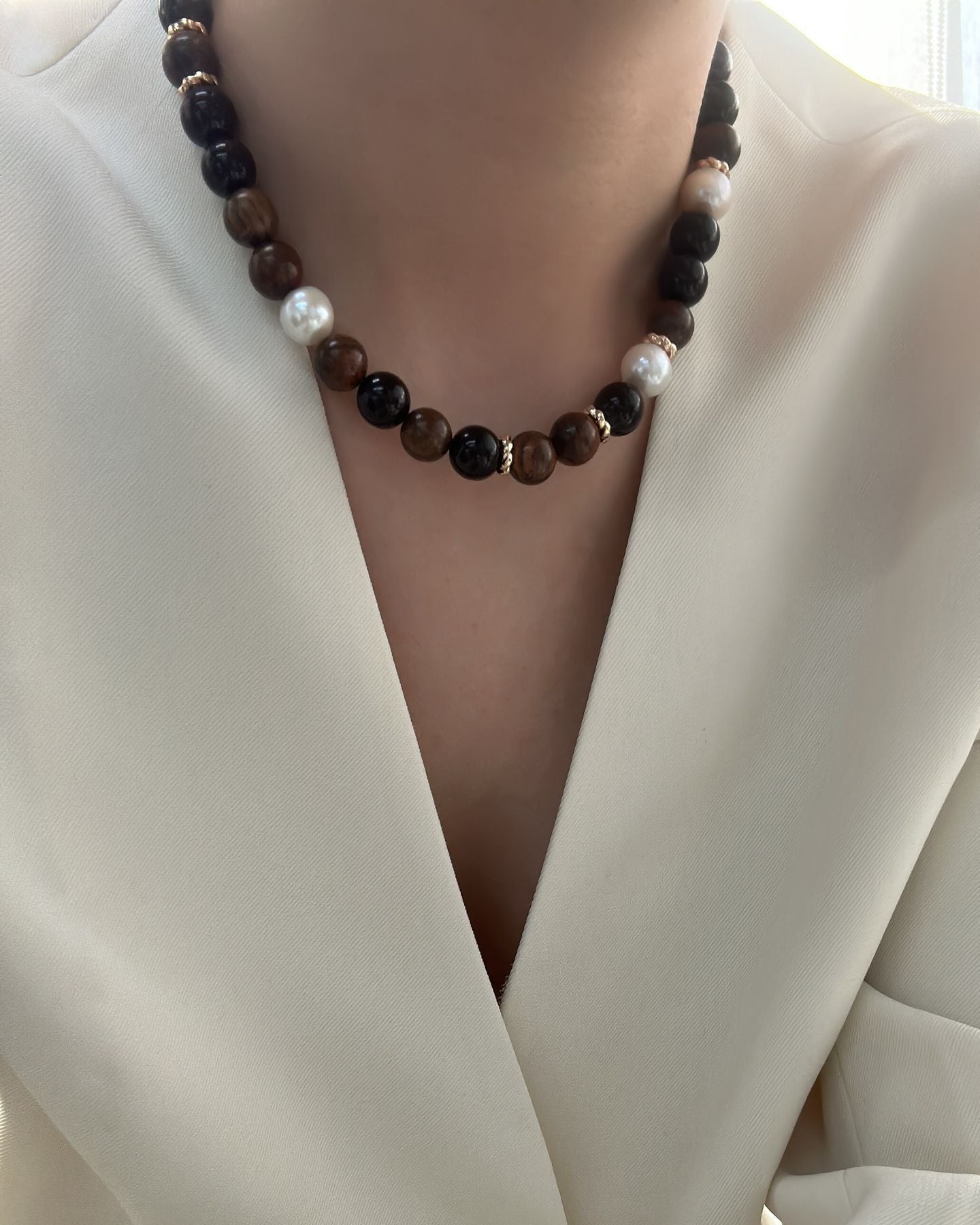 Person wearing a white outfit with a necklace featuring brown beads and pearls.