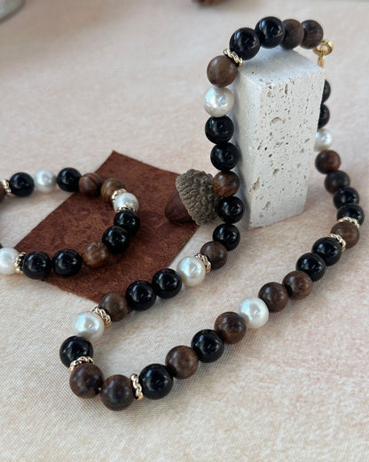 Beaded bracelets with black, brown, and pearl beads on a beige surface.