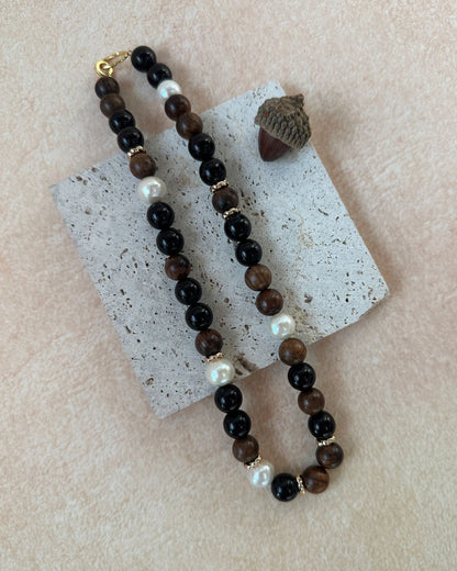Necklace with brown beads and pearls on a textured beige surface