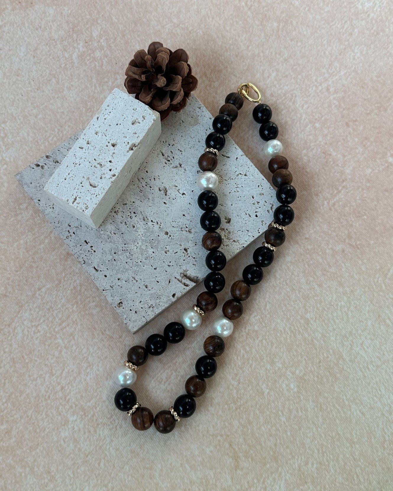 Beaded necklace with brown and white beads on a concrete block with a pine cone.