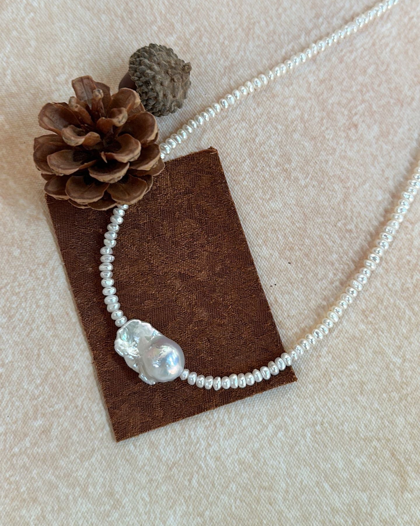 Pearl necklace with a pendant on a brown card with pine cones on a beige background