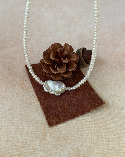 Pearl necklace with a decorative bead on a brown square pad with pinecones.