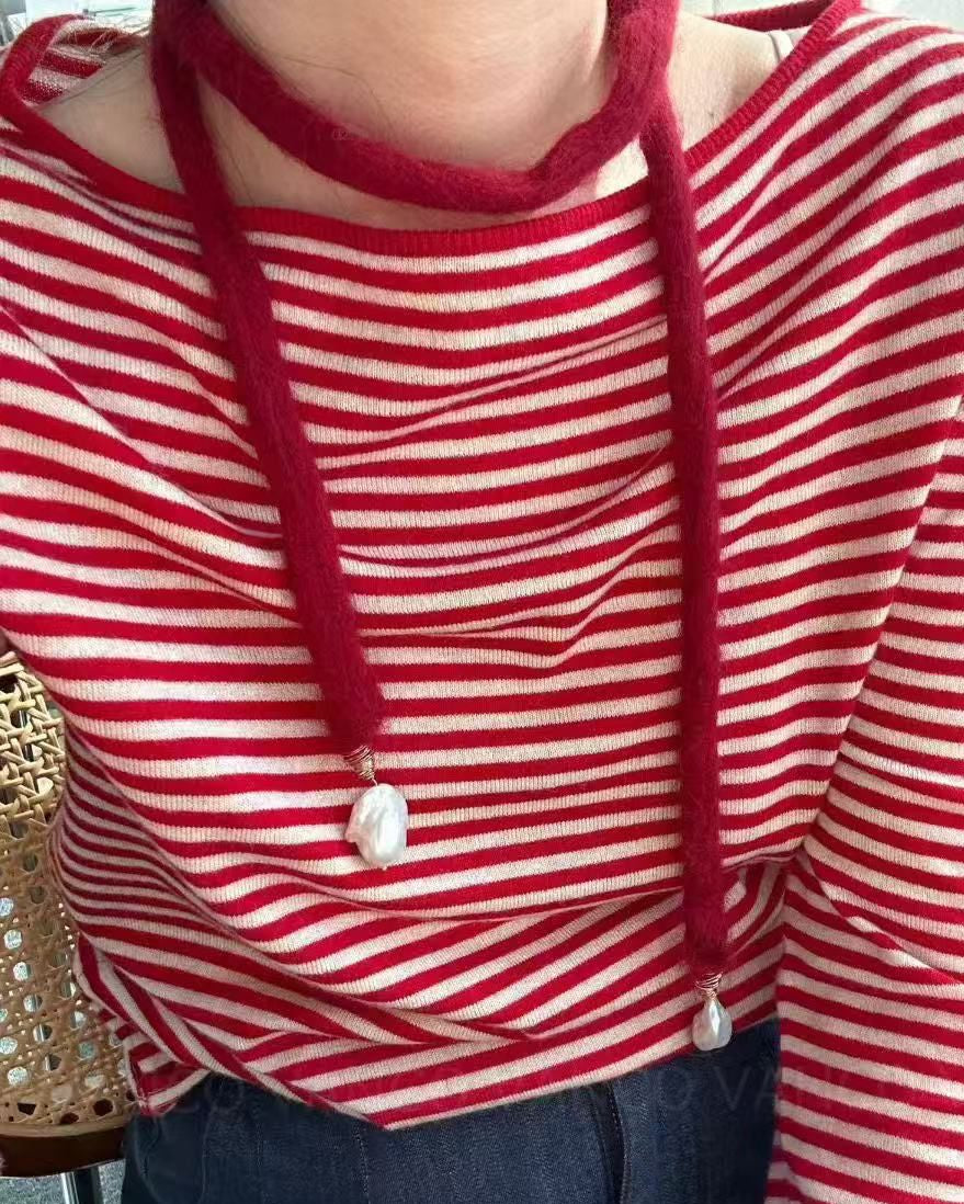 Person wearing a red and white striped shirt with a necklace, sitting on a chair.
