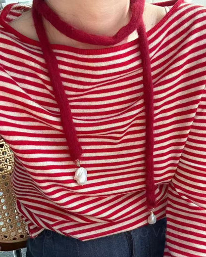 Person wearing a red and white striped shirt with a necklace, sitting on a chair.
