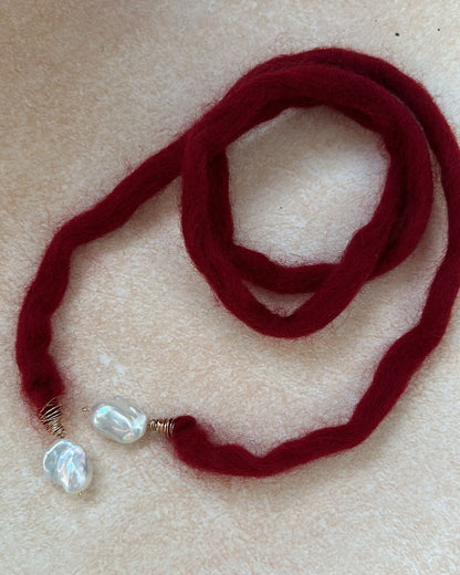 Red necklace with pearl-like beads on a beige surface