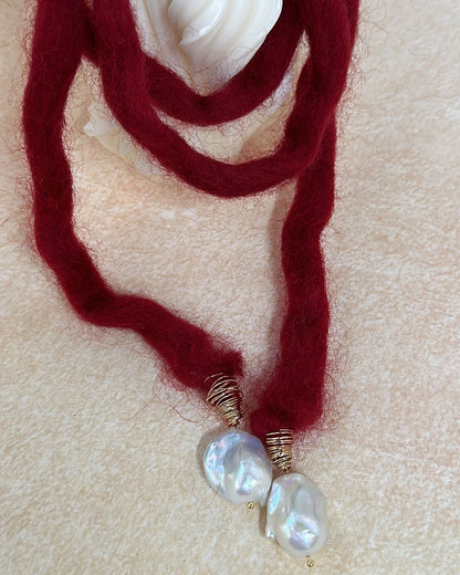 Red yarn necklace with pearl-like beads on a beige background