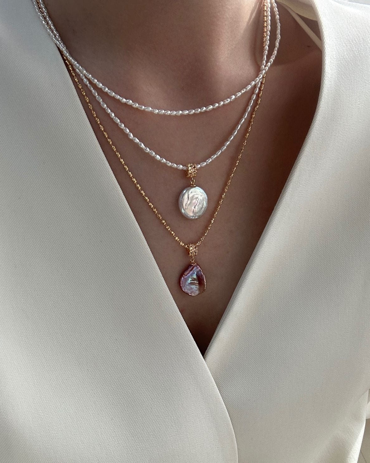 Close-up of a person wearing multiple necklaces with a white garment.