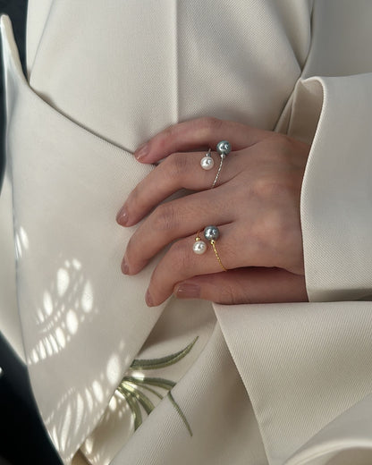 Close-up of hands wearing pearl rings on a light-colored garment.