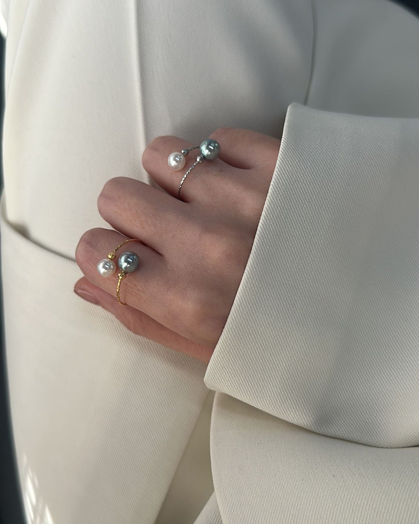 Close-up of a hand wearing multiple rings with pearls against a light-colored suit background