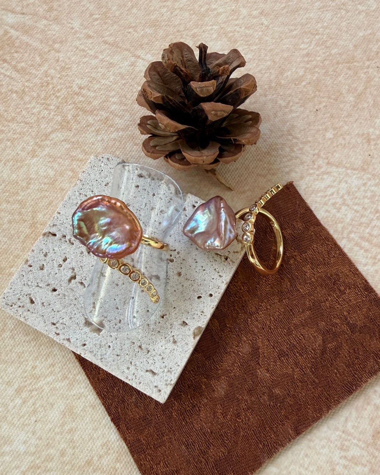 Pair of earrings on a card with a pine cone and brown fabric square on a beige background