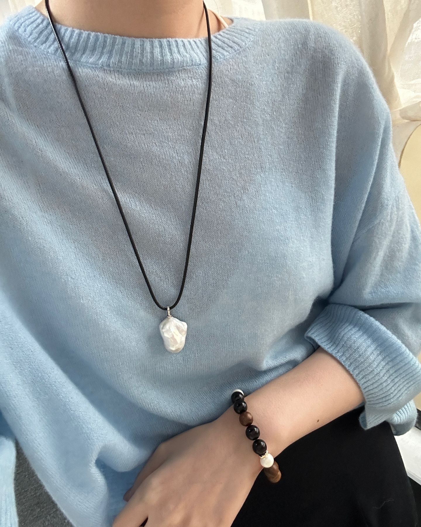 Person wearing a light blue sweater with a necklace and bracelet, blurred background