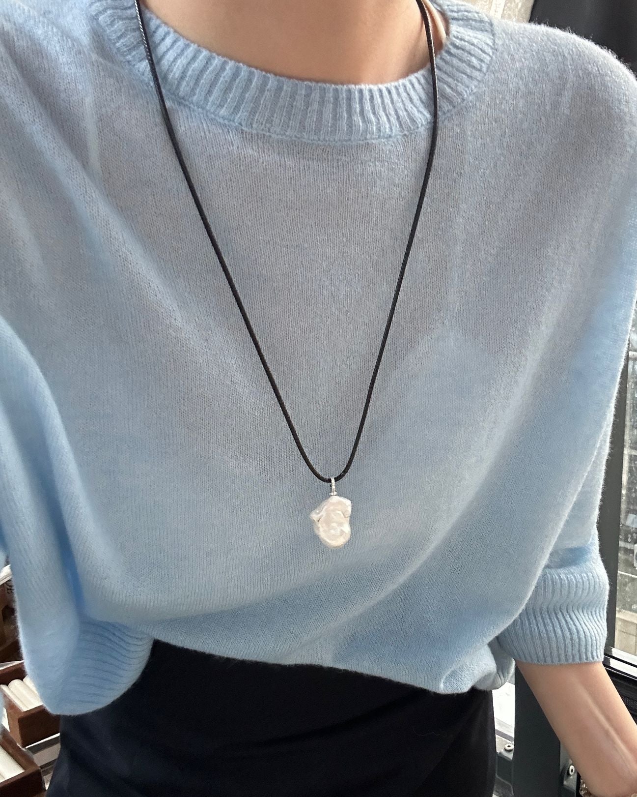 Person wearing a light blue sweater with a necklace featuring a shell pendant.