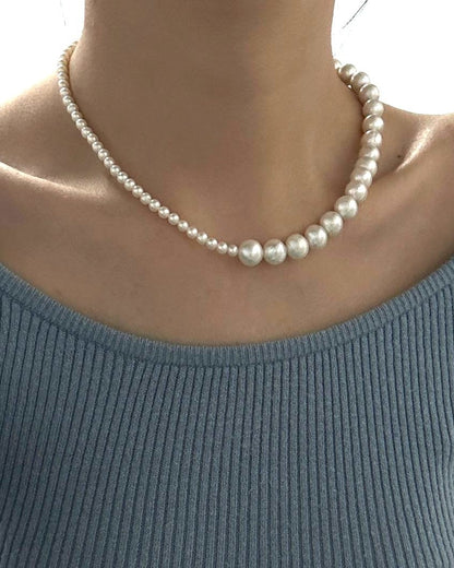 Person wearing a light blue sweater and pearl necklace in an indoor setting