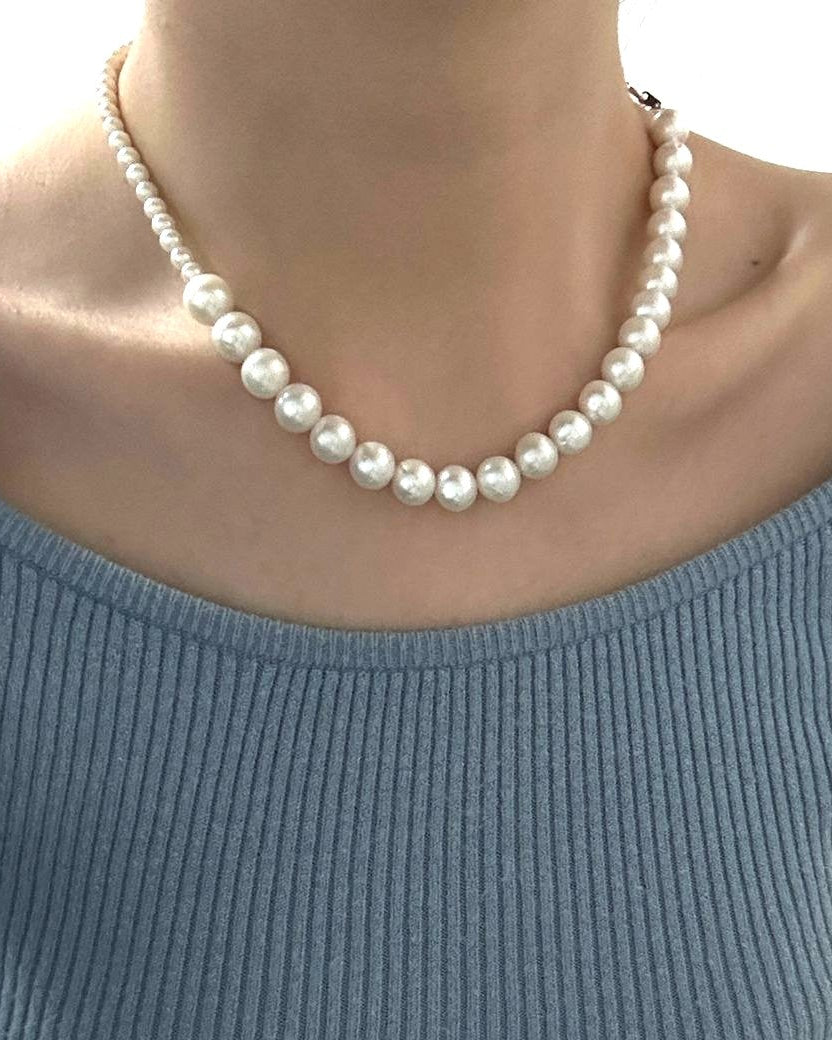 Person wearing a blue sweater and pearl necklace indoors