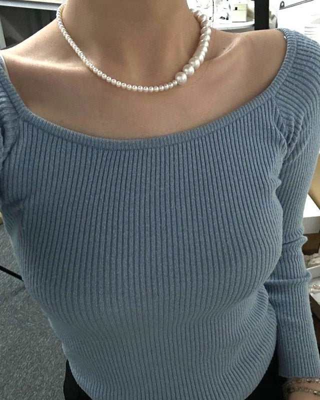 Person wearing a light blue sweater with a pearl necklace in an indoor setting