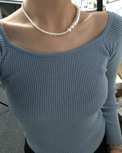 Person wearing a light blue sweater with a pearl necklace in an indoor setting